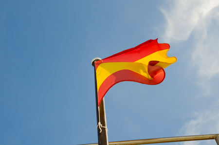 A vibrant red and yellow Spanish flag, blowing in the wind isolated on a vibrant blue sunny sky...