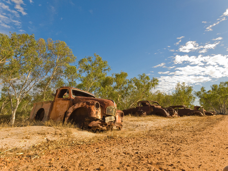 Rusty old australian vehicles in a sun drenched arid landscape. A car graveyard against the vibrant famous orange sand in the western australian desert.の写真素材