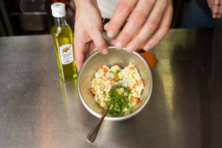 london, england, 05/05/2016, A metal stainless steel mixing bowl,  full of mashed organic carrot, potato, celeriac and parsley, being seasoned with salt and pepperの写真素材