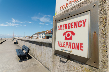An retro old weathered and distressed emergency telephone sign, on a rustic seaside wall near the...