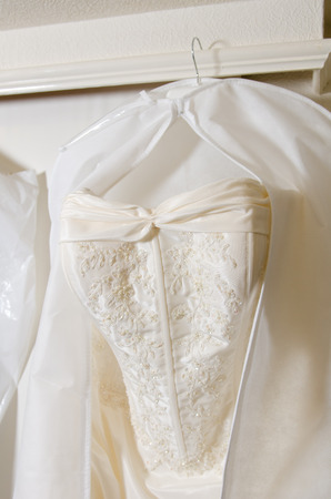 A beautiful cream and clean Wedding dress Hanging in front of a Window in a hotel room.の写真素材
