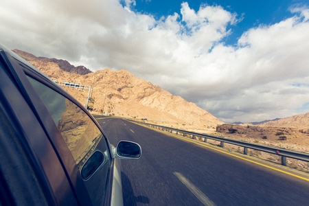 A road trip point of view of a road and car on a highway desert, point of view from someone hanging...