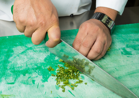 A bunch of organic fresh parsley, being finely sliced and chopped on a green citing board in a kitchen setting.の写真素材