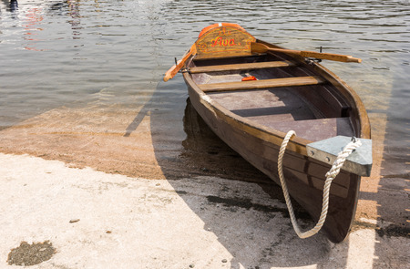 A wooden, vintage rustic rowing boat by the side of a lake.