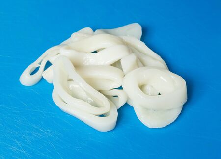A sliced fresh whole squid calamari ring pile, on a blue plastic fish cutting board.の写真素材