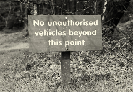 A no unauthorised vehicles beyond this point, hand carved wooden warning parking sign, on a stake with a countryside background. Sepia tones.の写真素材