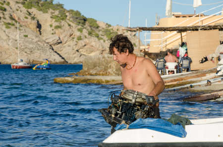ibiza, spain, 02/02/2016, A Spanish hippy man in ibiza, fixing his engine on his fishing boat. the man is in the water, preparing the boat for a fishing trip.のeditorial素材