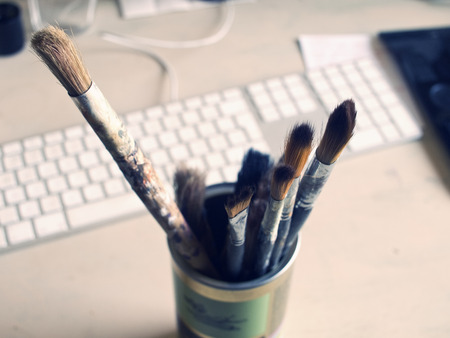 Old worn Rustic artistic artists paintbrushes, in a metal tin, with a keyboard in the background. Analogue and digital contrast.の写真素材