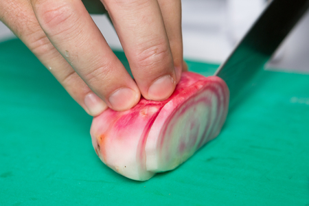 A hand chopping very pale fresh organic beetroot into slices in a kitchen on a green vegetable chopping board.の写真素材