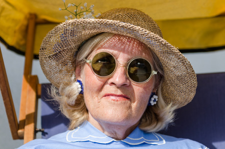 london, England, 05/05/2017, A stylish retro vintage fashionable old woman with blue clothing, retro sun glasses, vintage straw hat, and a rosette, in a Best dressed award at a vintage event..のeditorial素材