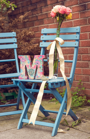 A very beautiful wooden 3d letter M, and a beautiful bouquet of colourful roses, on a blue wooden chair. A letter from the alphabet, the letter Mの写真素材