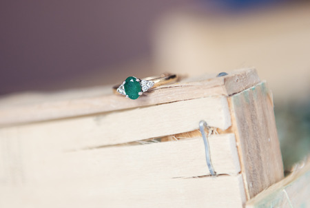 A beautiful expensive green emerald wedding ring with tiny diamonds on a rustic wooden bohemian background. Photographed with a shallow depth of field.の写真素材