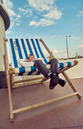 london, England, 05/05/2017, A stylish retro vintage fashionable man sat relaxing with arms on head, on a giant retro seaside deckchair. Giant deckchair. Best dressed award. のeditorial素材