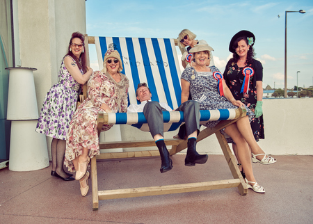 london, England, 05/05/2017, A group of stylish retro vintage fashionable people sat on a giant retro seaside deckchair. Giant deckchair. Best dressed award. のeditorial素材