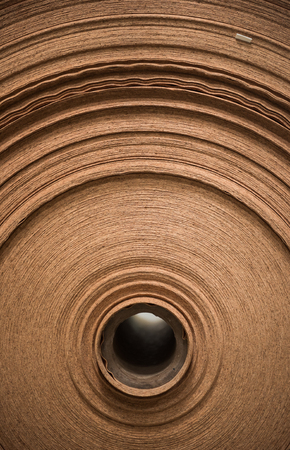 A beautiful smooth clean paper roll machine creating a continuous sheet of brown freshly made paper for painting, wallpaper and wrapping. Industrial paper roll folds on industrial machinery.の写真素材