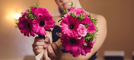 A beautiful bridesmaid holding a bouquet of warm pink beautiful organic natural flowers into the camera with a shallow depth of field. conceptual image for a wedding celebration.の写真素材