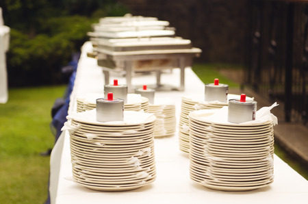 A stack of empty clean white buffet banquet crockery plates on a whit stable at an outdoor event in...