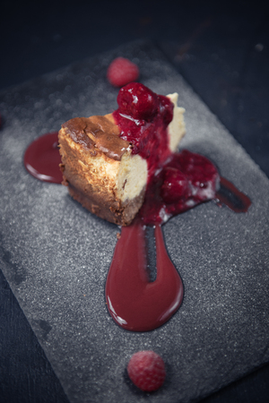 A raspberry and strawberry cheesecake slice dessert served on a rustic gray fashionable hipster slate plate. Dark food photography.の写真素材