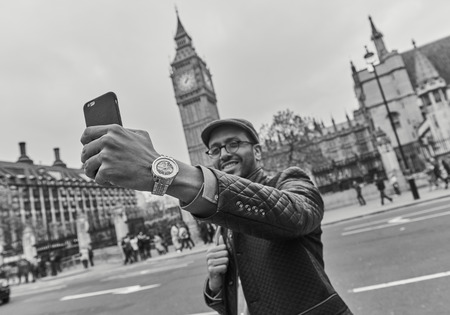 london, england, 05/05/2018 A male tourist taking selfie photos with his mobile phone outside the world famous london landmark big ben in westminster.のeditorial素材