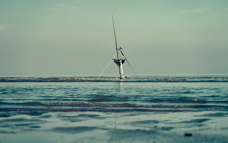 A beautiful cinematic scene of a fisherman fishing off the beach with a line and pole , with a dark...