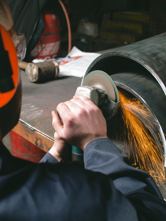A man working with a grinder in a factory, creating sparks. metal working apparent angle grinding metal and steel parts. matte dark photography.の写真素材