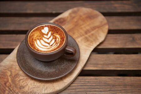 A beautiful creamy brown warm fresh cappuccino coffee cup, full of creamy coffee, served in a wooden rustic brown coffee shop with coffee art.の写真素材