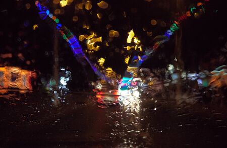 Abstract painterly rain drops on a car window with vibrant city and street lights out of focus in...