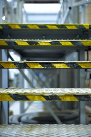 london, england, 05/05/2018 An industrial metal steel stair case in an urban factory setting. Futuristic post apocalyptic environment. Yellow hazard tape for health and safety incase of slipping and falling.の写真素材