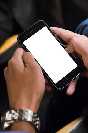 Mockup image of mans hands holding an empty smart phone, mobile phone with blank screen on thigh sat...