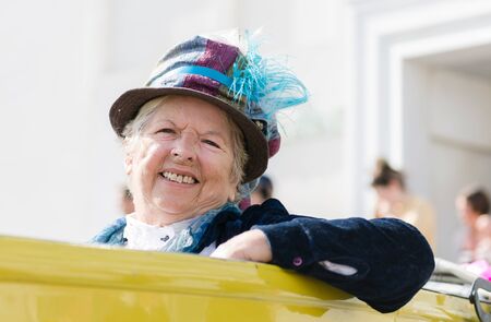 london, england, 10/11/2018 An old lady sat driving in an old vintage car vehicle. Dressed in nostalgic vintage clothing and unusual fashion sense.のeditorial素材