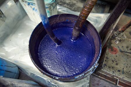 A vibrant large pot of blue and aqua mixed acrylic block printing and screen printing paint in a bucket in an industrial creative art studio setting. Artists ink mix in an art studio.の写真素材