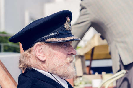london, England, 05/05/2017, An scruffy old bearded sailor man on a rainbow coloured seaside vintage deck chair. Hipster costume seafarer. nautical captain of a boat with a sailor hat.のeditorial素材