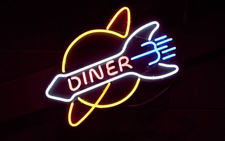 A vintage retro american style neon sign advertising a diner. A dark setting with neon tube lighting up the dark in red. Food advertising and signage in the food industryの写真素材