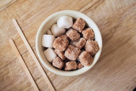 Abowl of brown crystallised sugar cubes from above, in a hipster coffee shop on a rustic brown table, photographed with a shallow depth of field. Sugar cubes perfect for tea and coffee hot drinks.の写真素材