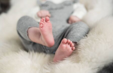 A beautiful soft delicate warm young baby foot photographed with a shallow depth of field. gentle calm colours and feel. baby care and well being. babies feet on a cream fur rug.の写真素材