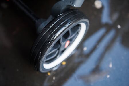 A baby pram stroller pushchair wheel tyre,  in a wet rainy dirty city sidewalk pavement environment. City strollers, and fashionable baby pram accessories for city living parents. modern parent hood.の写真素材