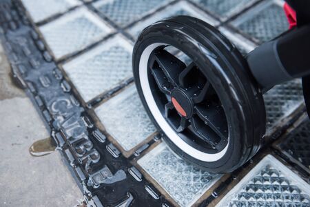 A baby pram stroller pushchair wheel tyre,  in a wet rainy dirty city sidewalk pavement environment....
