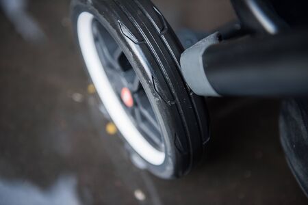 A baby pram stroller pushchair wheel tyre,  in a wet rainy dirty city sidewalk pavement environment. City strollers, and fashionable baby pram accessories for city living parents. modern parent hood.の写真素材