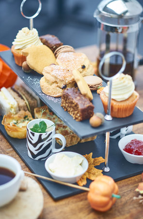 A beautiful gourmet selection of english afternoon tea cakes and scones served with organic cupcakes, tea and coffee, strawberry jam and clotted cream. traditional british food.の写真素材