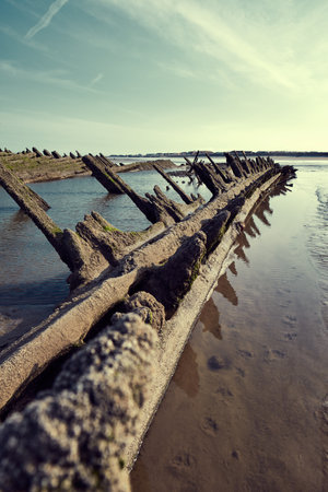 An old historic wooden shipwreck vessel carcass exposed on a desolate tropical island beach. Maritime and exploration disaster. Pirate boats from historical days. Beached ship wrecksの写真素材