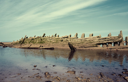 An old historic wooden shipwreck vessel carcass exposed on a desolate tropical island beach. Maritime and exploration disaster. Pirate boats from historical days. Beached ship wrecksの写真素材