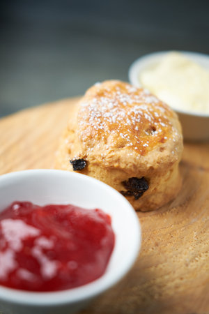 A beautiful gourmet scone served with tea and coffee, strawberry jam and clotted cream. traditional british food. Cackes and see treatsの写真素材