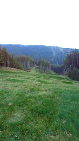 Vertical panoramic image of mountain meadow. Ski slope in Beskydy in summer. Fresh green grass with forests and hills in the background.の写真素材