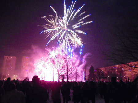 Red crackling fireworks and yellow fire rockets exploding with bursts of light and noise over crowded area on New Year Eve.の写真素材
