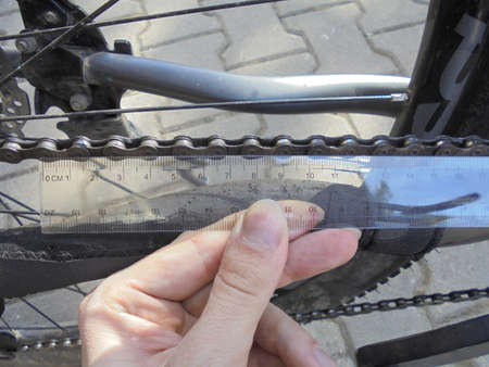 Close view on manual checking of bike chain wear and tear degree by measuring the length of segments with a transparent plastic ruler.の写真素材