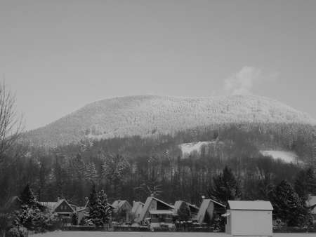 Blackwhite image - Majestic mountain scene, Czech hill Ostra Hora in Beskydy and its dense spruce forest coated in snow, towering over several small village houses.の写真素材