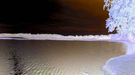 Negative image - Beautiful nature scene with peaceful pond with calm water under partly cloudy sky and shining sun causing light damage due to overexposition.の写真素材