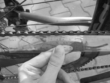 Blackwhite image - Close view on manual checking of bike chain wear and tear degree by measuring the length of segments with a transparent plastic ruler.の写真素材