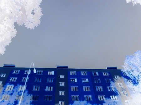 Negative image - Image of large block of flats illuminated by evening sunshine, but with dark cloud above itself. Time after storm in city.の写真素材