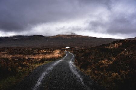 Road will guide you. Isle of Skye. Single white house in under the moody mountain top hidden in Scotland April 2019の写真素材